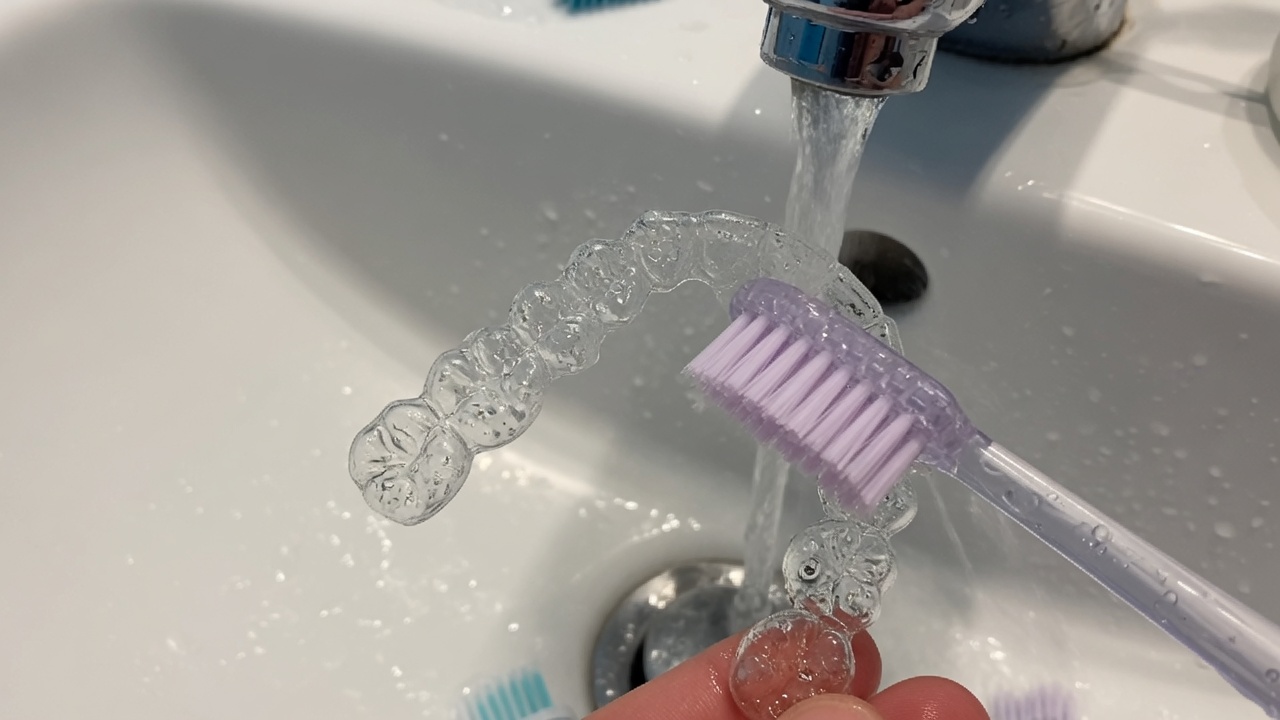 Nettoyage d’une gouttière dentaire d’alignement à l’eau tiède au-dessus d’un lavabo